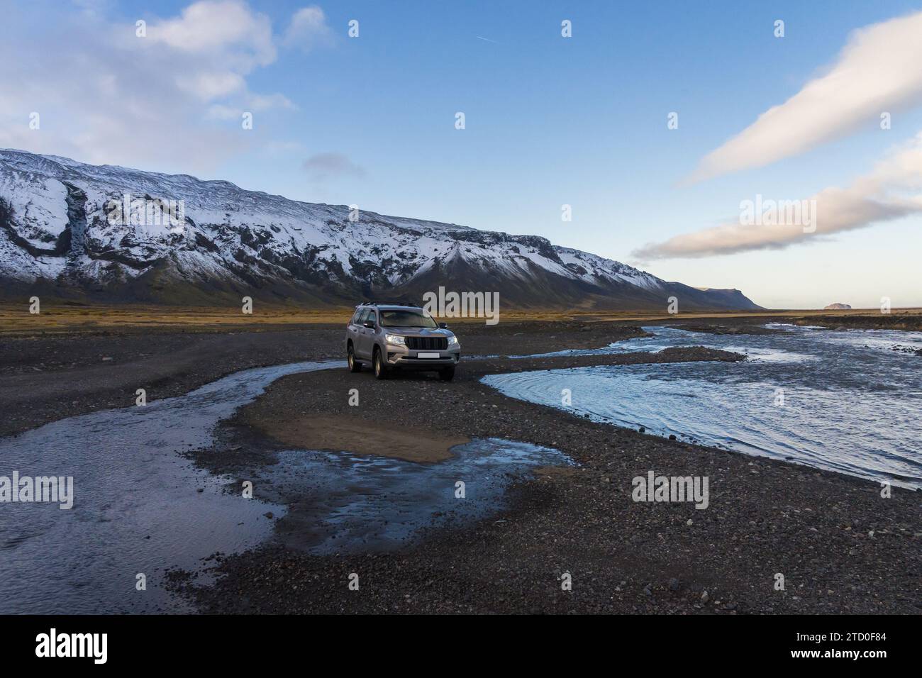 Un véhicule tout-terrain parcourt une rivière peu profonde dans la vallée de Thorsmork, au milieu de montagnes enneigées sous un ciel bleu avec des nuages dans les Highlands islandais Banque D'Images