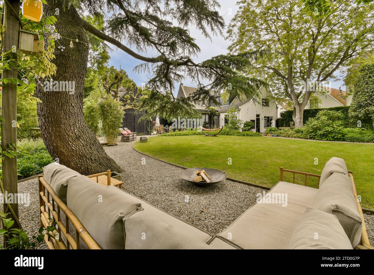 Canapé confortable avec foyer sur le patio par pelouse herbeuse entourée d'arbres luxuriants avec villa contemporaine en arrière-plan Banque D'Images