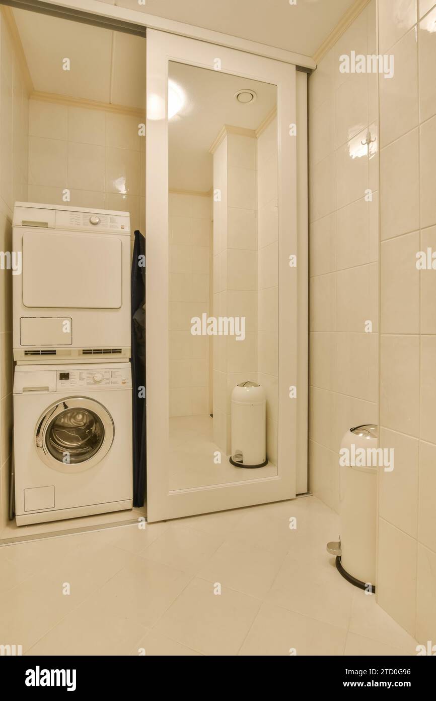 Lave-linge et sèche-linge par cabine de douche avec porte coulissante dans la salle de bains blanche moderne à la maison Banque D'Images
