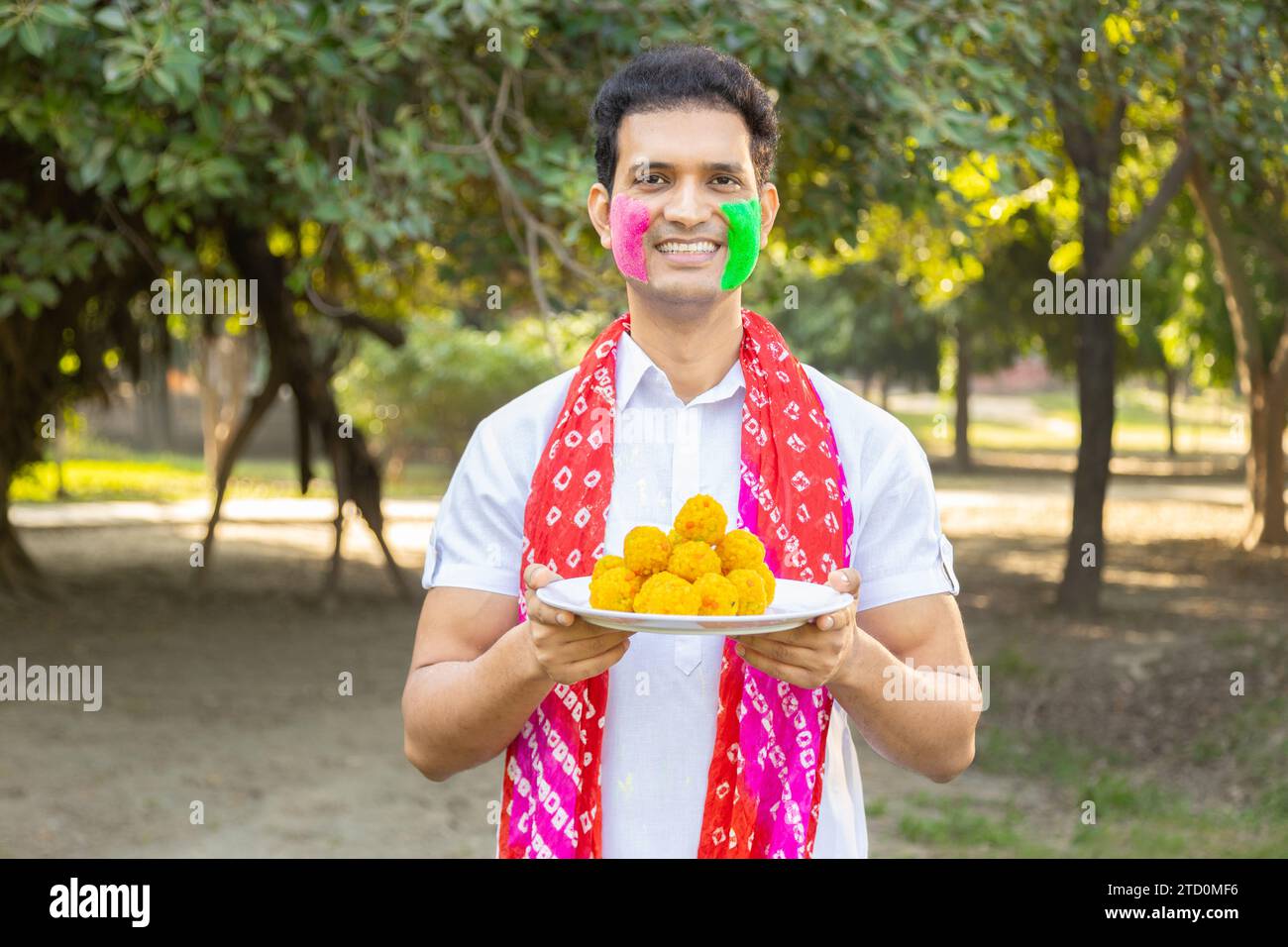 Jeune indien portant kurta blanc tenant une assiette de motichoor ladoos. Célébration du festival Holi dans le parc ou le jardin. Banque D'Images
