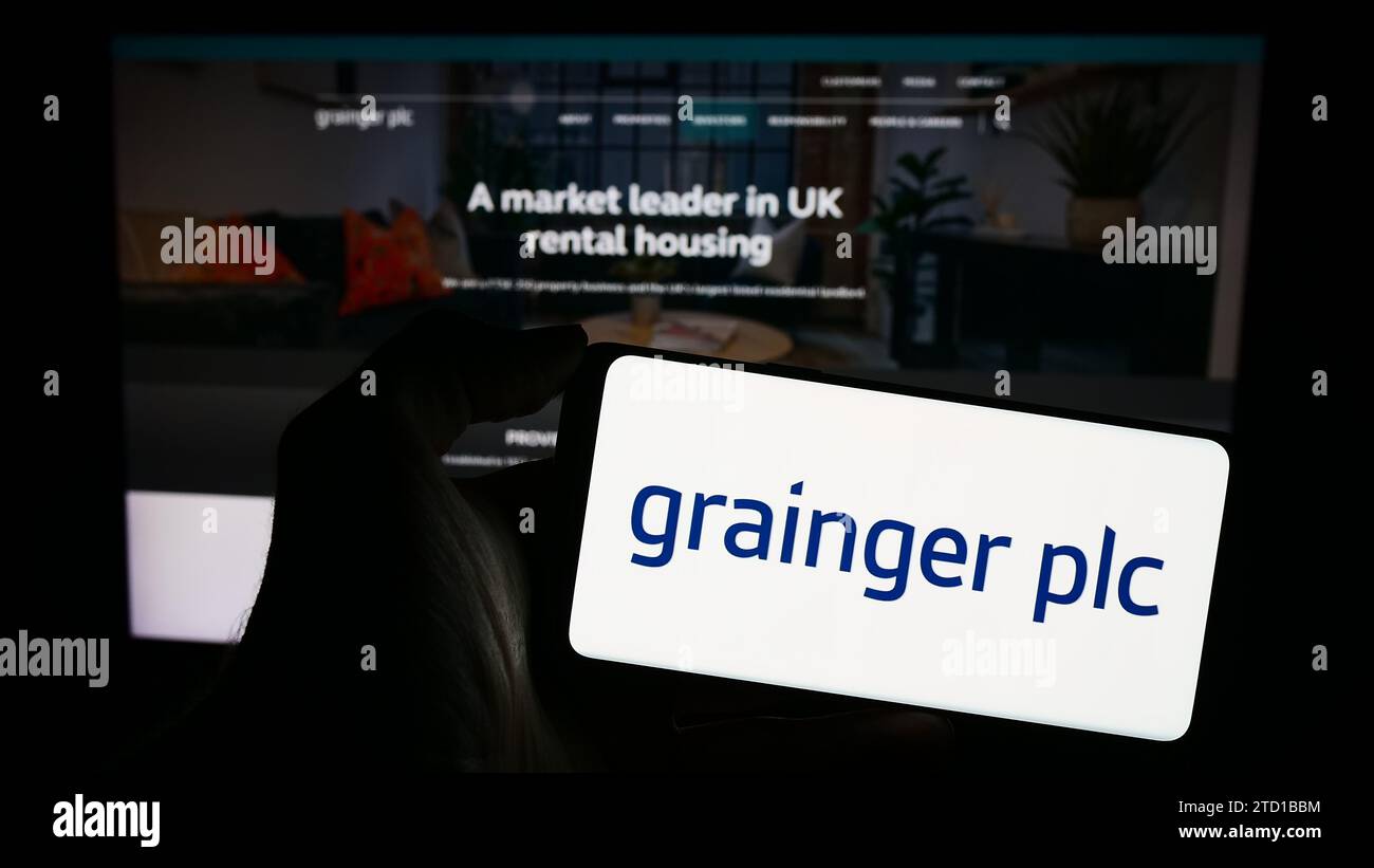 Personne tenant le téléphone portable avec le logo de la société immobilière résidentielle britannique Grainger plc devant la page Web de l'entreprise. Concentrez-vous sur l'affichage du téléphone. Banque D'Images