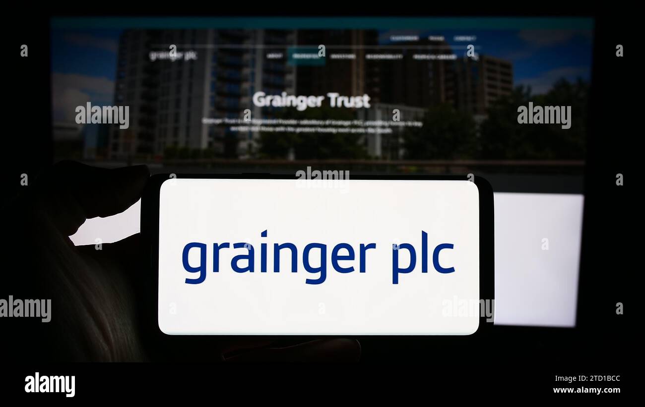 Personne détenant un smartphone avec le logo de la société immobilière résidentielle britannique Grainger plc devant le site Web. Concentrez-vous sur l'affichage du téléphone. Banque D'Images