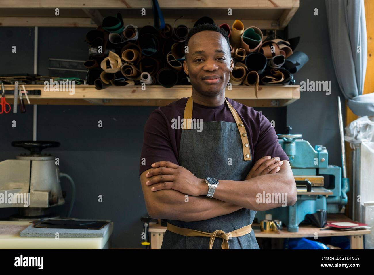 Un jeune homme se tient debout dans son atelier de cuir où il conçoit et fabrique des articles de mode tels que des sacs suspendus, des portefeuilles et des ceintures. Banque D'Images