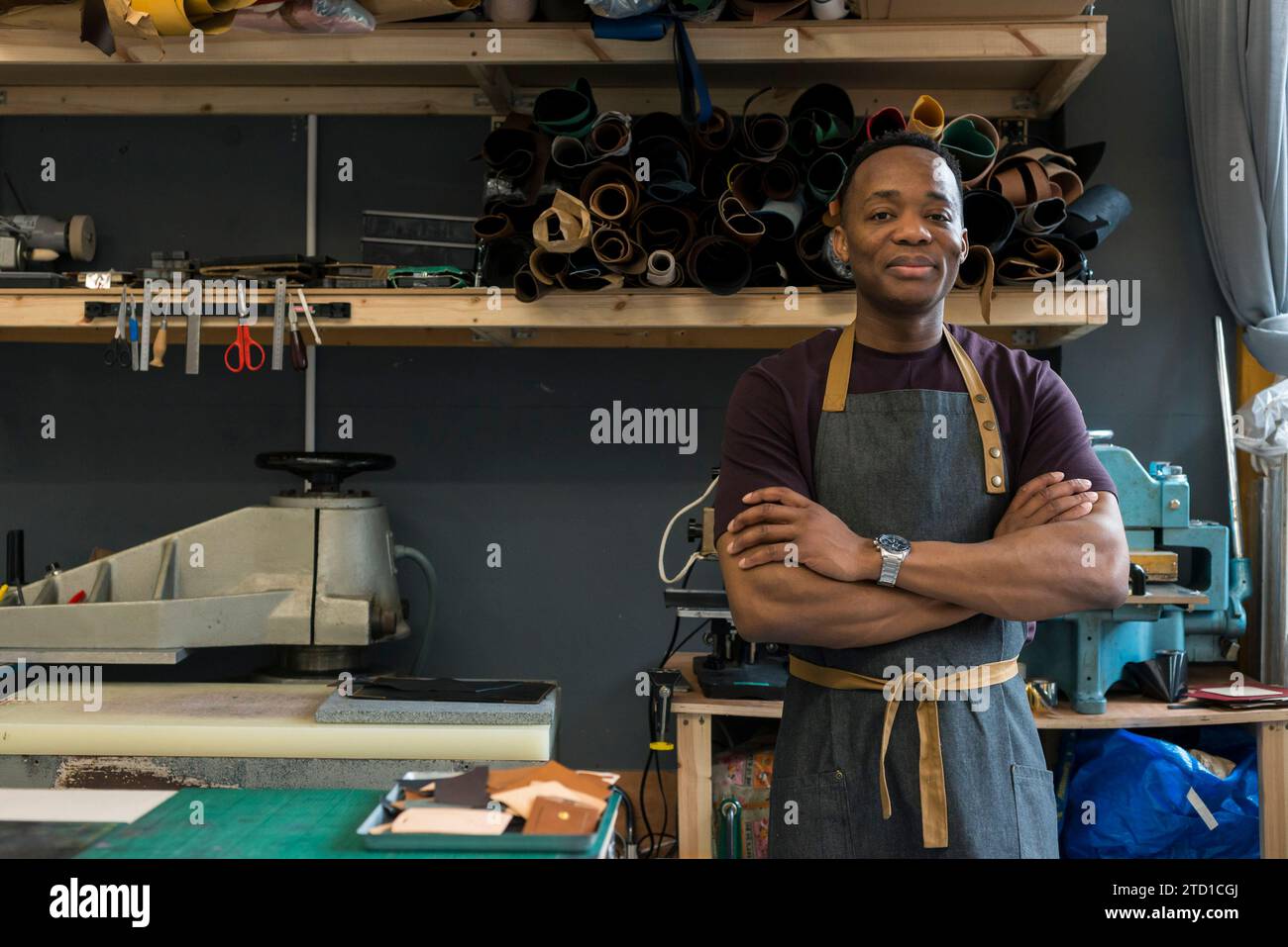 Un jeune homme se tient debout dans son atelier de cuir où il conçoit et fabrique des articles de mode tels que des sacs suspendus, des portefeuilles et des ceintures. Banque D'Images