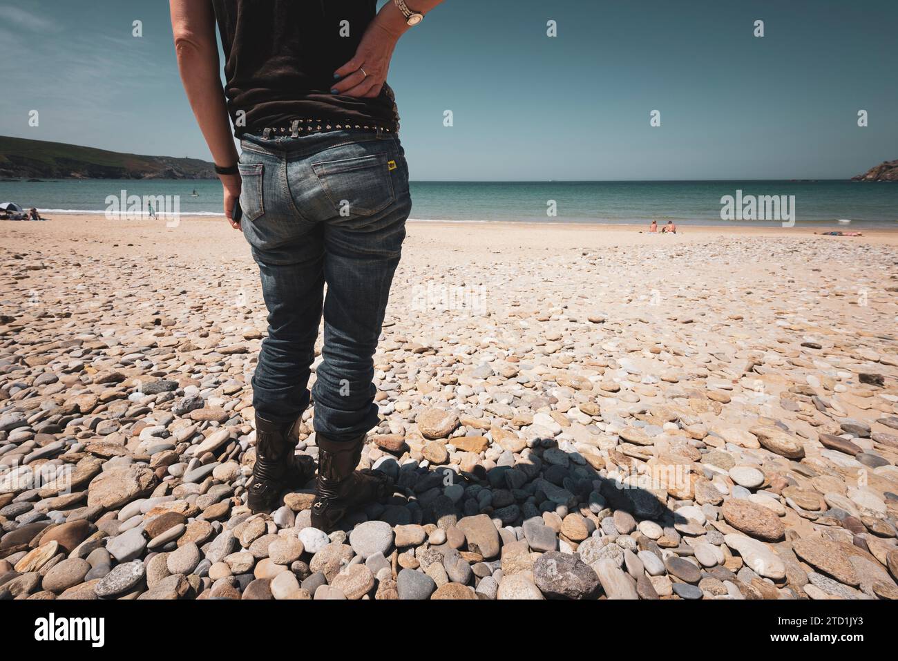Une femme portant des vêtements et des bottes de moto se tient sur la plage de galets de Plage des Trespasses en Bretagne France Banque D'Images