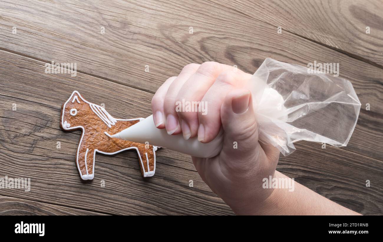 Mignon cheval en pain d'épice ou main humaine avec sac à passepoil sur fond en bois brun. Gros plan de décoration de biscuits cuits au four sucrés en forme de poney par glaçage blanc. Banque D'Images