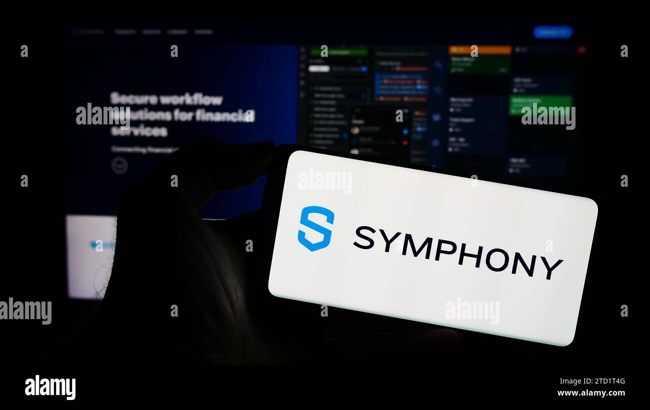 Personne tenant le téléphone portable avec le logo de la société de messagerie américaine Symphony communication Services LLC en face de la page Web. Concentrez-vous sur l'affichage du téléphone. Banque D'Images