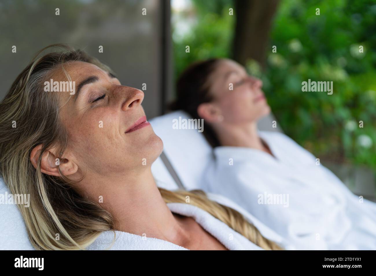 Deux femmes se relaxant sur des chaises longues en plein air, l'une au foyer avec les yeux fermés. Image concept d'hôtel spa bien-être Banque D'Images