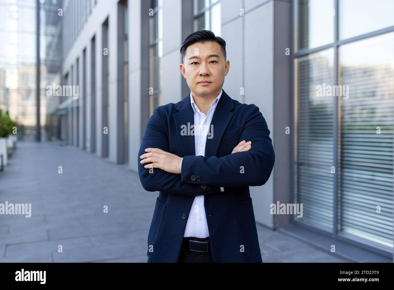 Portrait d'un jeune avocat asiatique, homme d'affaires debout à l'extérieur d'un immeuble de bureaux dans un costume, les bras croisés sur sa poitrine, regardant sérieusement et con Banque D'Images