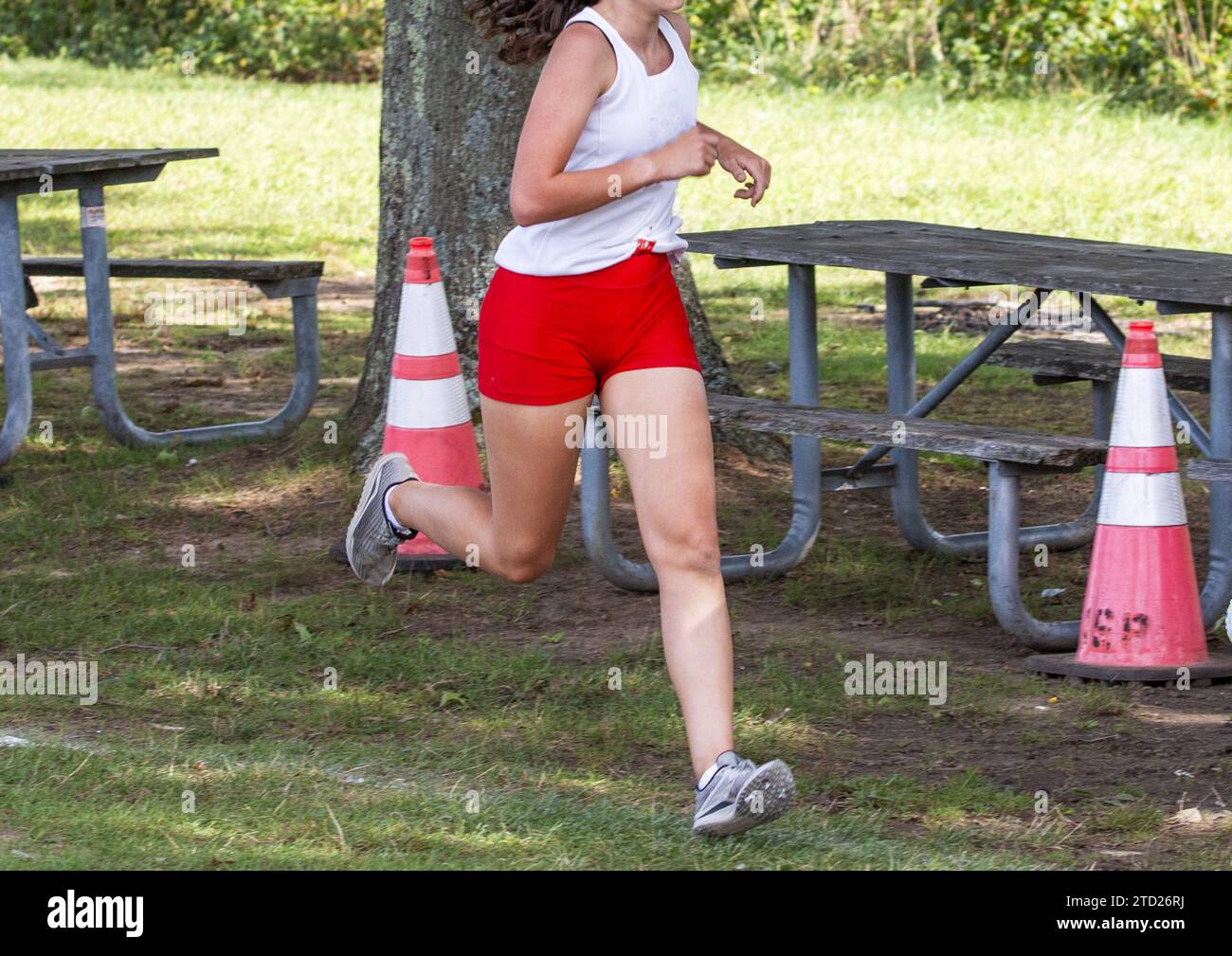 Une femme en short rouge et un débardeur blanc courant une course de 5k dans un parc. Banque D'Images