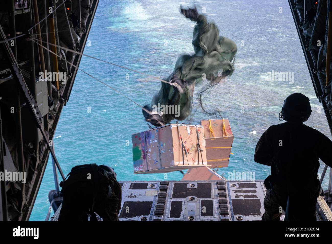 Oneop, Îles Mortlock, États fédérés de Micronésie. 03 décembre 2023. Ian Munoz, chef de chargement de l'US Air Force, regarde des paquets de fret humanitaire flotter vers un lagon en parachute depuis un C-130J Super Hercules de l'US Air Force pendant l'opération Christmas Drop, le 3 décembre 2023 à Oneop, Mortlock Islands, Micronésie. L’opération Christmas Drop est la plus ancienne mission humanitaire et de secours en cas de catastrophe qui fournit 71 000 livres de nourriture, de cadeaux et de fournitures pour aider les communautés insulaires éloignées du Pacifique Sud. Crédit : SRA Brooklyn Golightly/US Airforce photo/Alamy Live News Banque D'Images