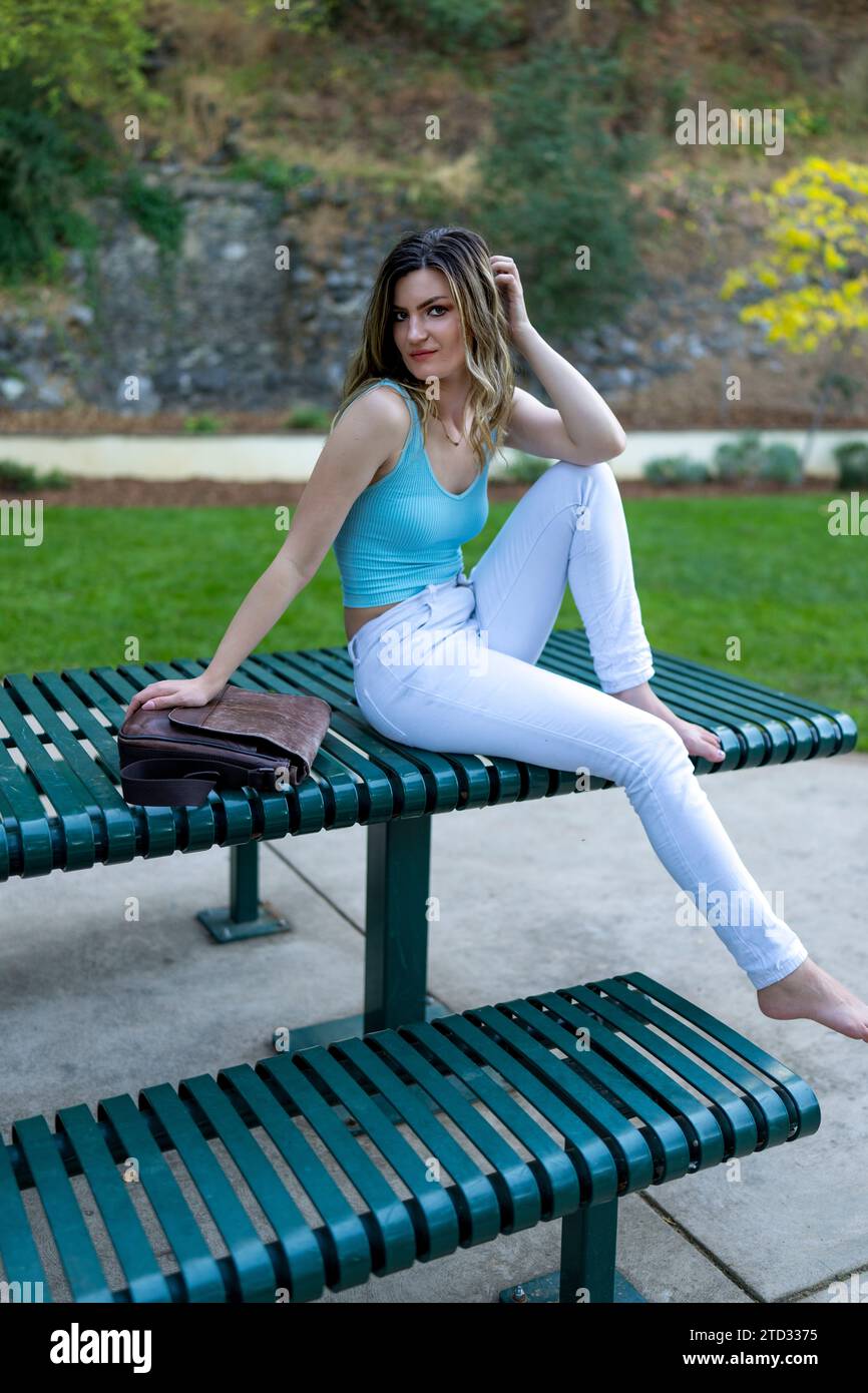 Heureuse jeune femme dans des couleurs vives assise sur Metal Park Table dans l'après-midi Banque D'Images