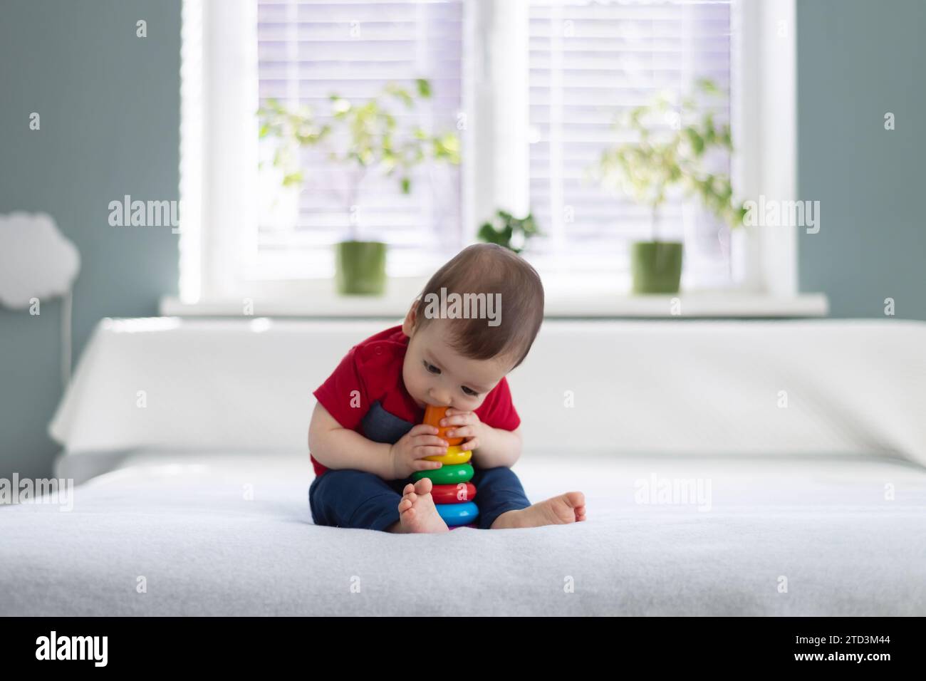 Petit garçon pieds nus en t-shirt rouge mangeant son jouet préféré pyramide colorée. Concept d'enfance heureuse Banque D'Images