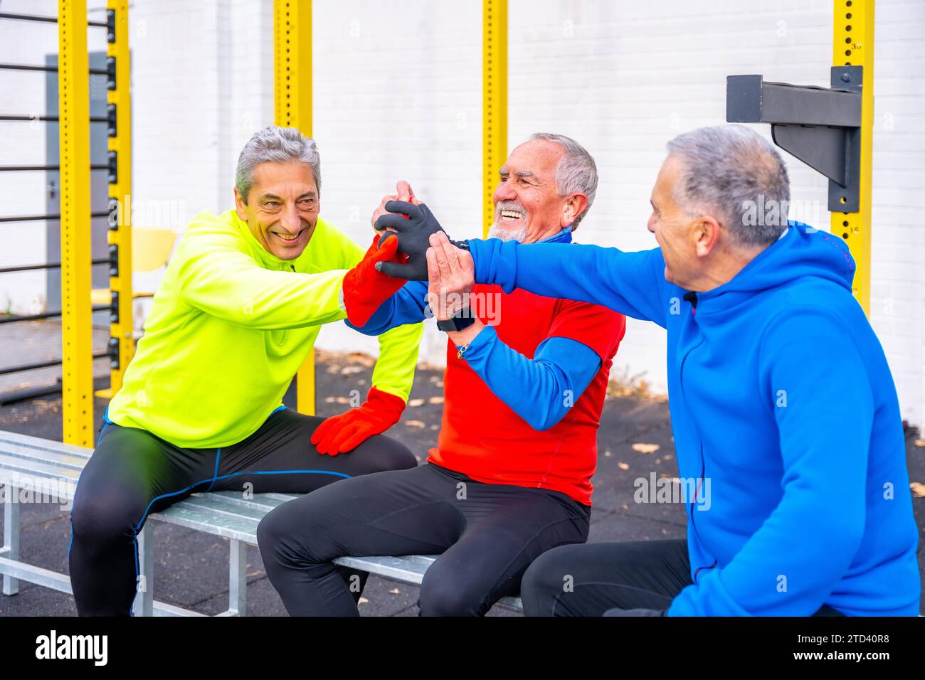 Trois hommes retraités âgés donnent cinq dans un terrain de jeu de sports en plein air Banque D'Images