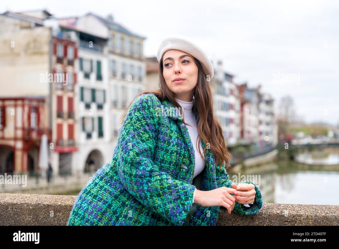 Jolie femme en béret debout à côté de la rivière tout en visitant la ville Banque D'Images
