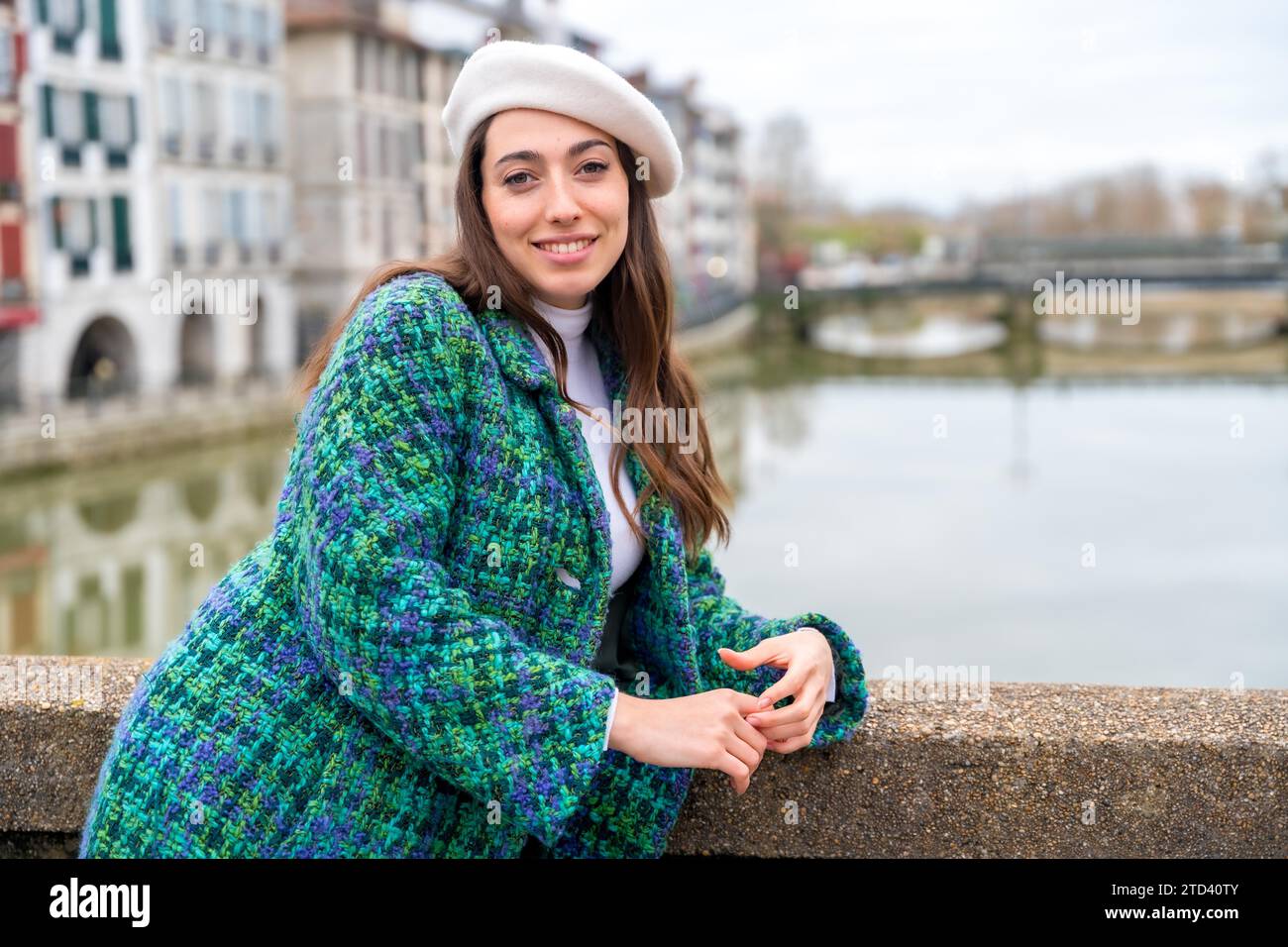 Femme chic portant manteau et béret souriant à la caméra penchée à côté de la rivière Banque D'Images