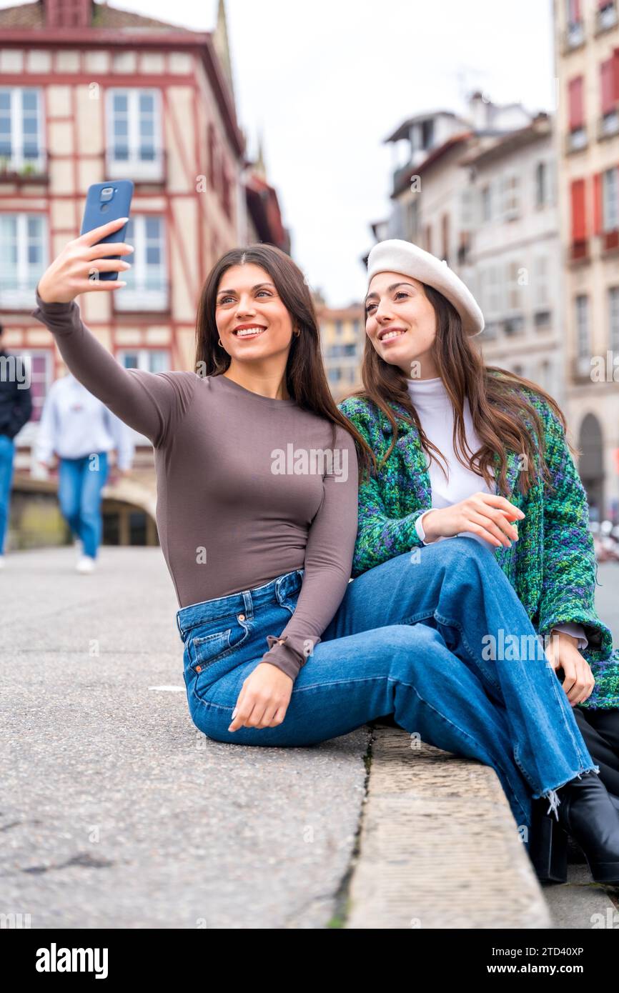 Photo verticale de deux amis élégants prenant un selfie assis sur une place de la ville Banque D'Images