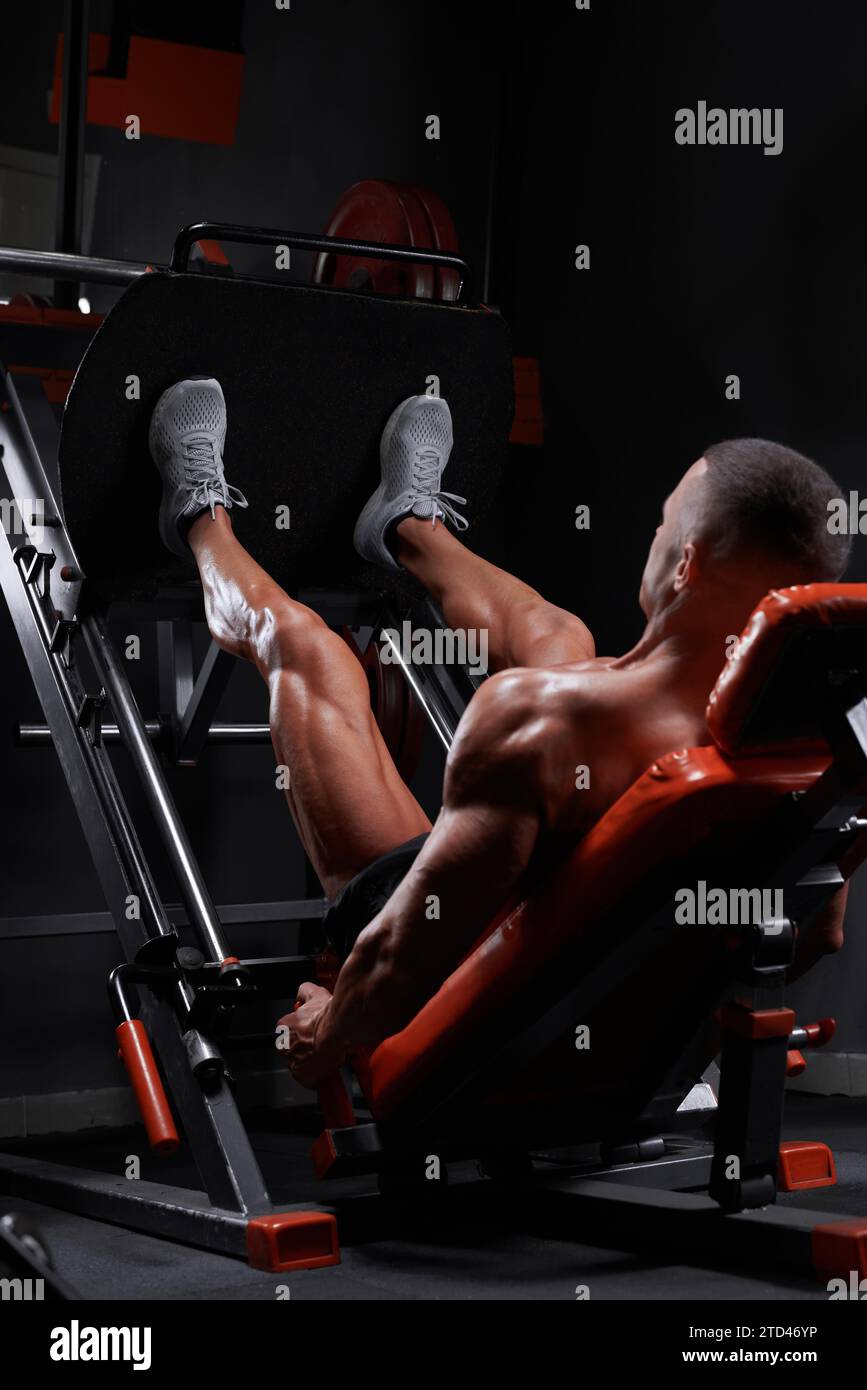 Vue latérale de l'athlète masculin ethnique musculaire allongé sur la machine de presse de jambe et pompant les muscles pendant l'entraînement dans la salle de gym. Supports mixtes Banque D'Images