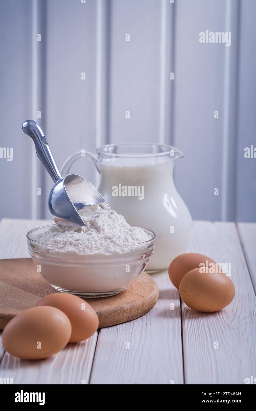 Œufs farine dans un bol transparent pichet avec du lait sur un vieux panneau en bois laqué blanc manger et boire concept Banque D'Images