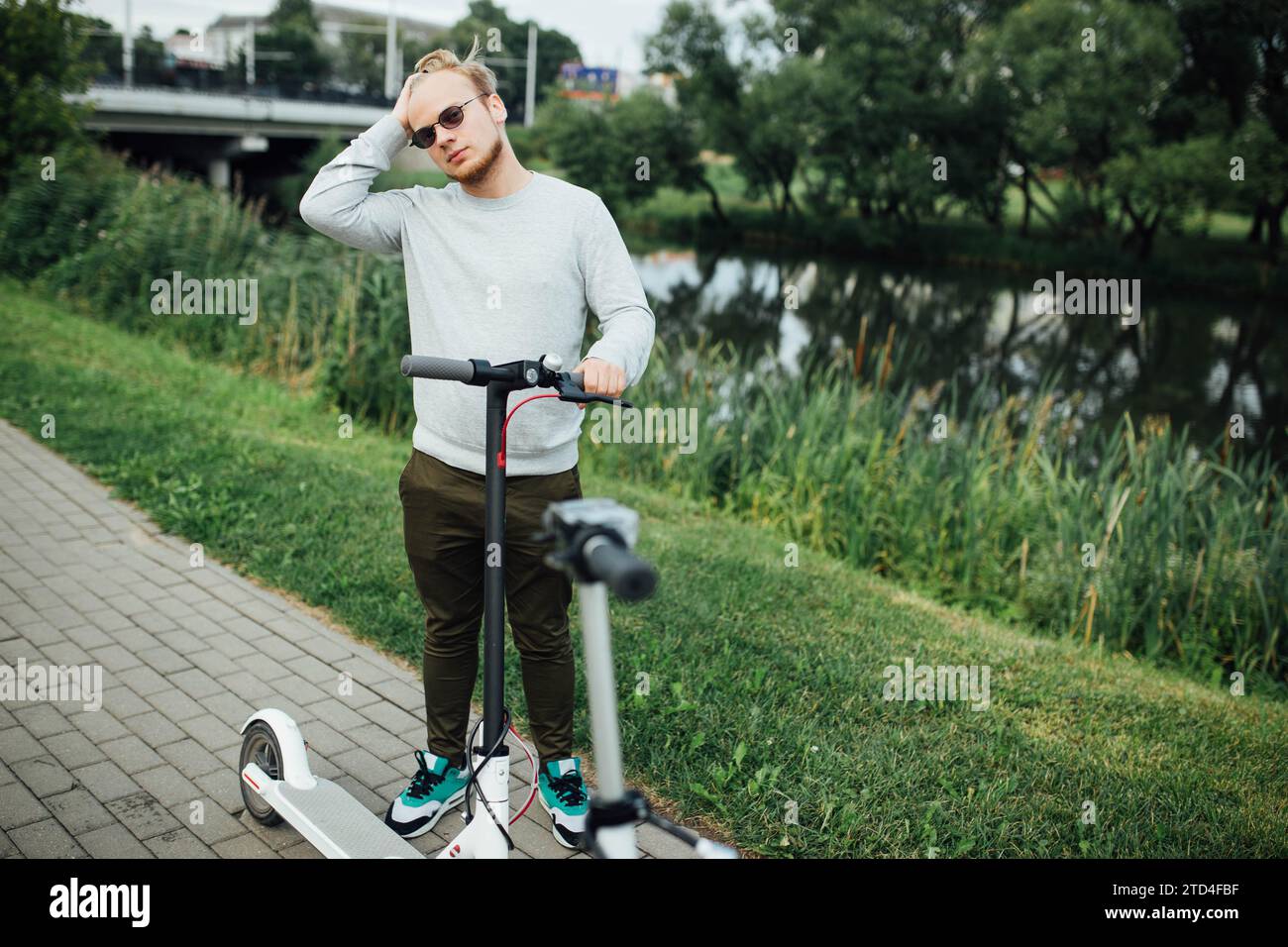 Jeune bel homme blond attend un ami pour partir en voyage sur des scooters électriques Banque D'Images