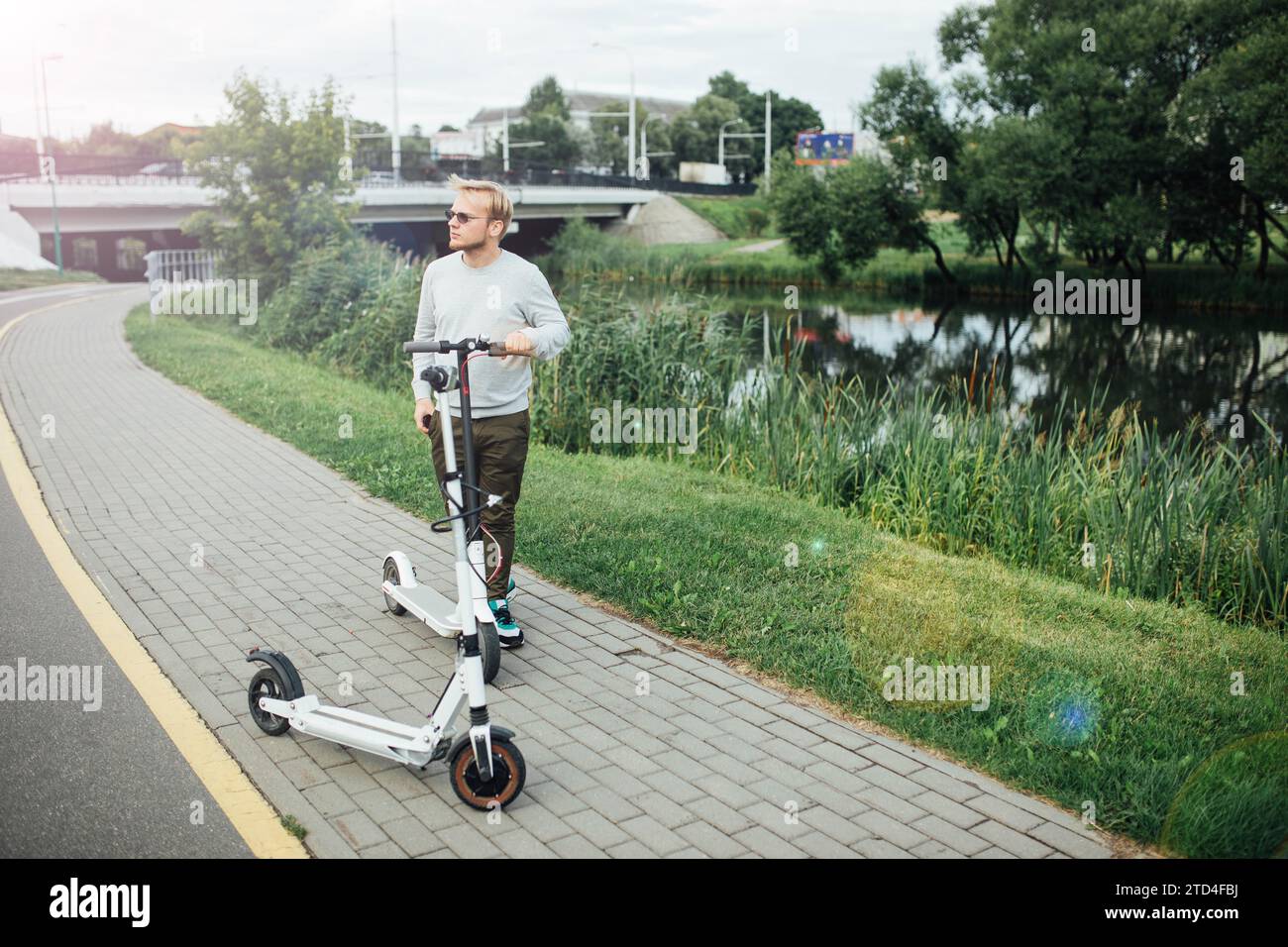 Jeune bel homme blond attend un ami pour partir en voyage sur des scooters électriques Banque D'Images