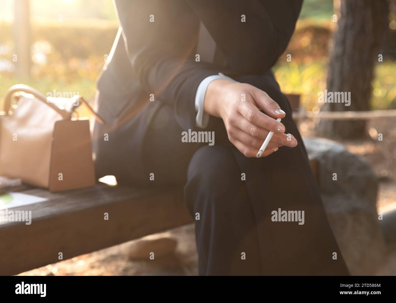 Une femme est assise sur un banc de parc et fume une cigarette Banque D'Images