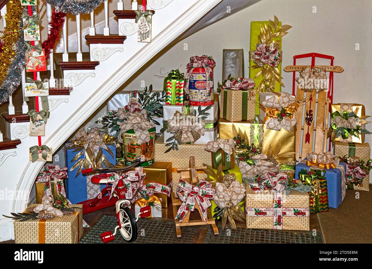 Cadeaux de Noël ; festive ; donner ; vacances ; cadeaux, sous l'escalier incurvé, emballages colorés, arcs, tricycle, cheval à bascule en bois, traîneau flexible Flyer Banque D'Images