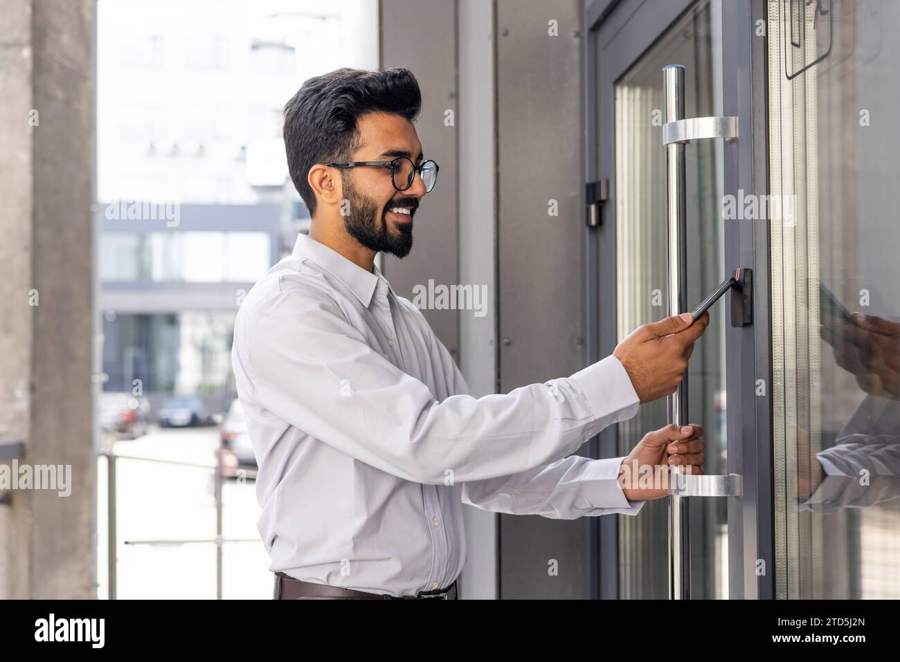 Jeune homme d'affaires utilisant le téléphone pour ouvrir la porte de bureau de l'immeuble, homme heureux utilisant l'accès sans fil, homme d'affaires allant au travail heureux souriant. Banque D'Images