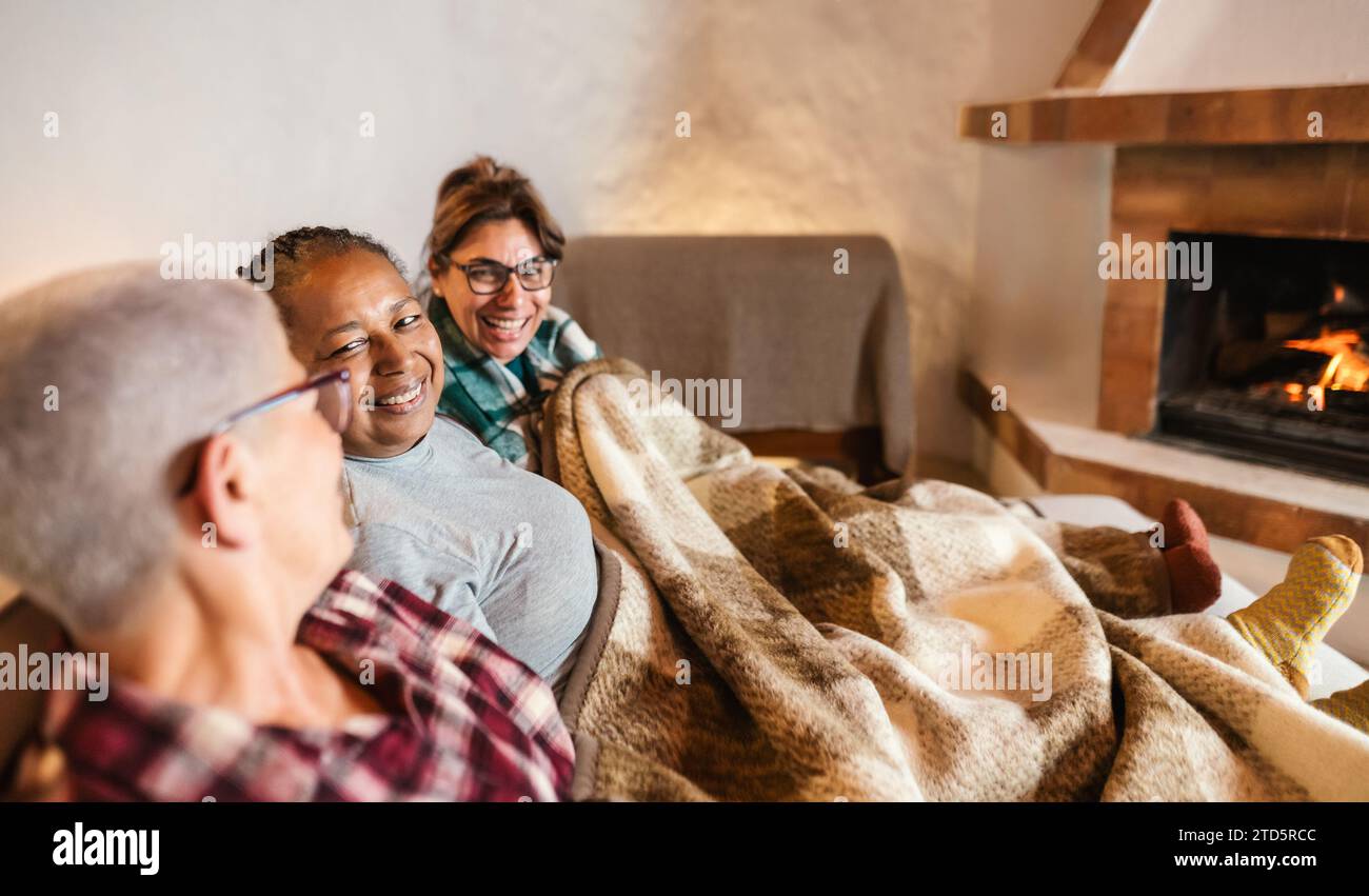 Femmes multiraciales heureuses ayant se détendre devant la cheminée dans une maison confortable - concept de saison de contenu d'hiver Banque D'Images