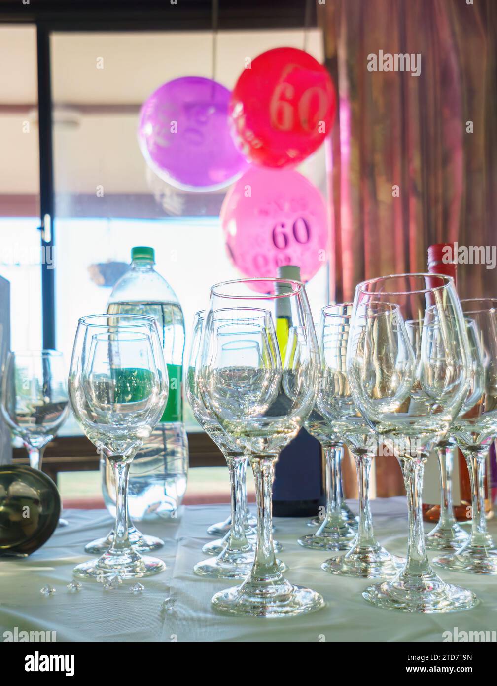 ballons du 60e anniversaire suspendus à la fenêtre, focalisation sélective sur les verres à vin sur la table. Fête d'anniversaire. Format vertical. Banque D'Images