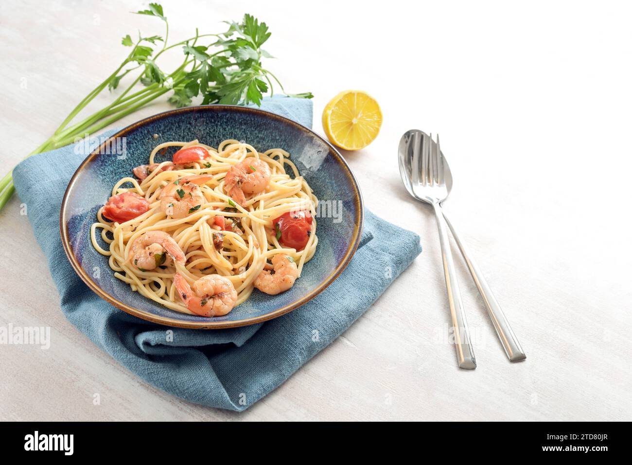 Spaghetti aux crevettes et tomates en sauce citron avec garniture de persil dans une assiette bleue sur une table en bois blanc, repas de fruits de mer méditerranéens maison, Banque D'Images