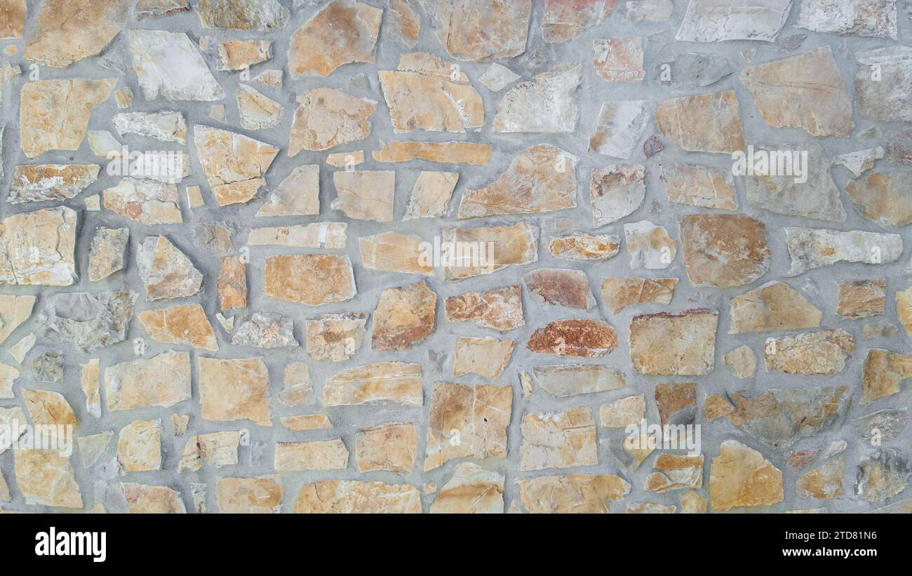 Mur de ciment texturé avec diverses pierres rugueuses et irrégulières en gris, beige et ocre. Idéal pour les arrière-plans Banque D'Images