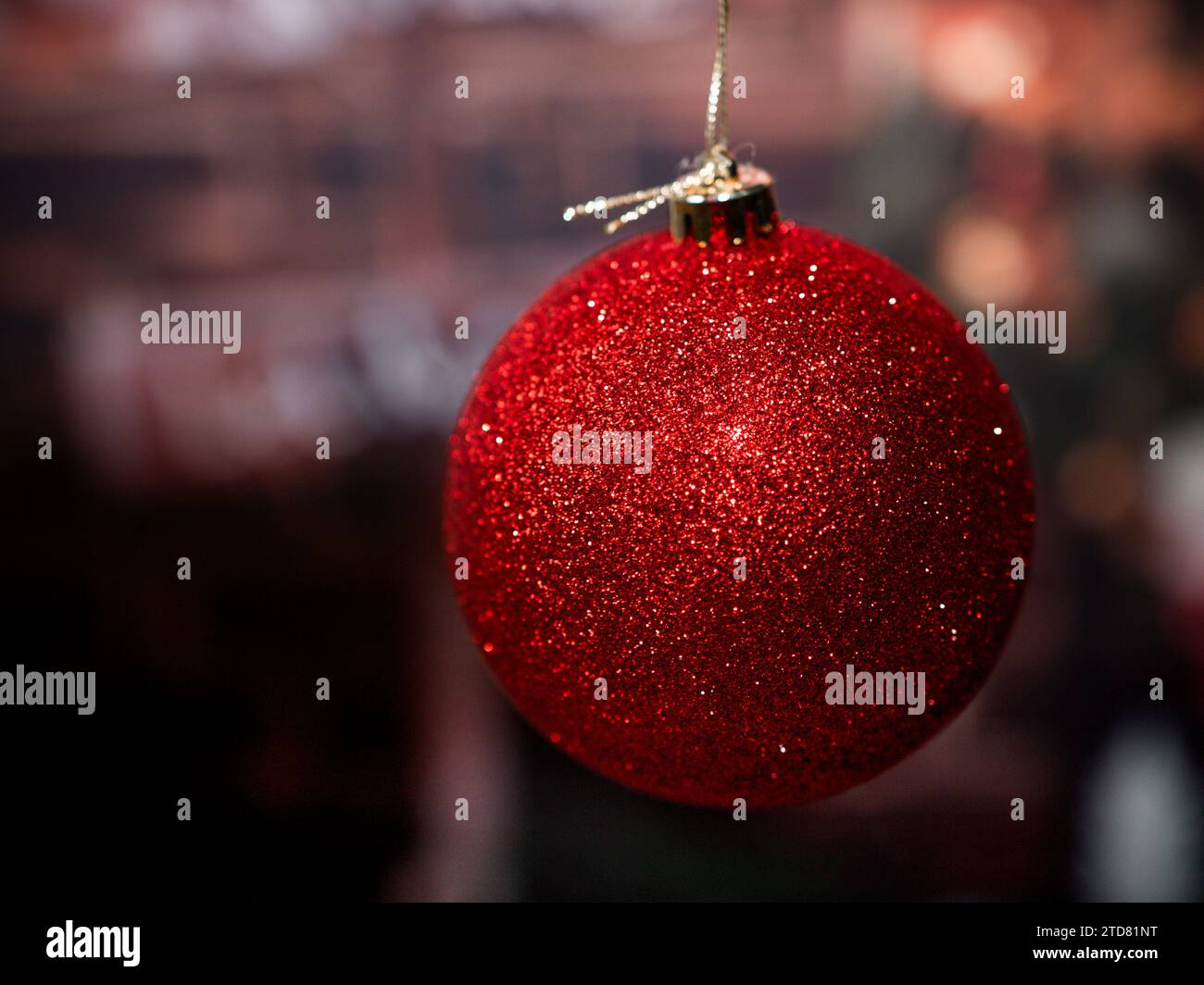 Une grosse boule de Noël rouge brillante accrochée à une ficelle dorée sur un fond flou de mauvaise humeur. Fond de saison des fêtes avec espace vide pour le texte Banque D'Images