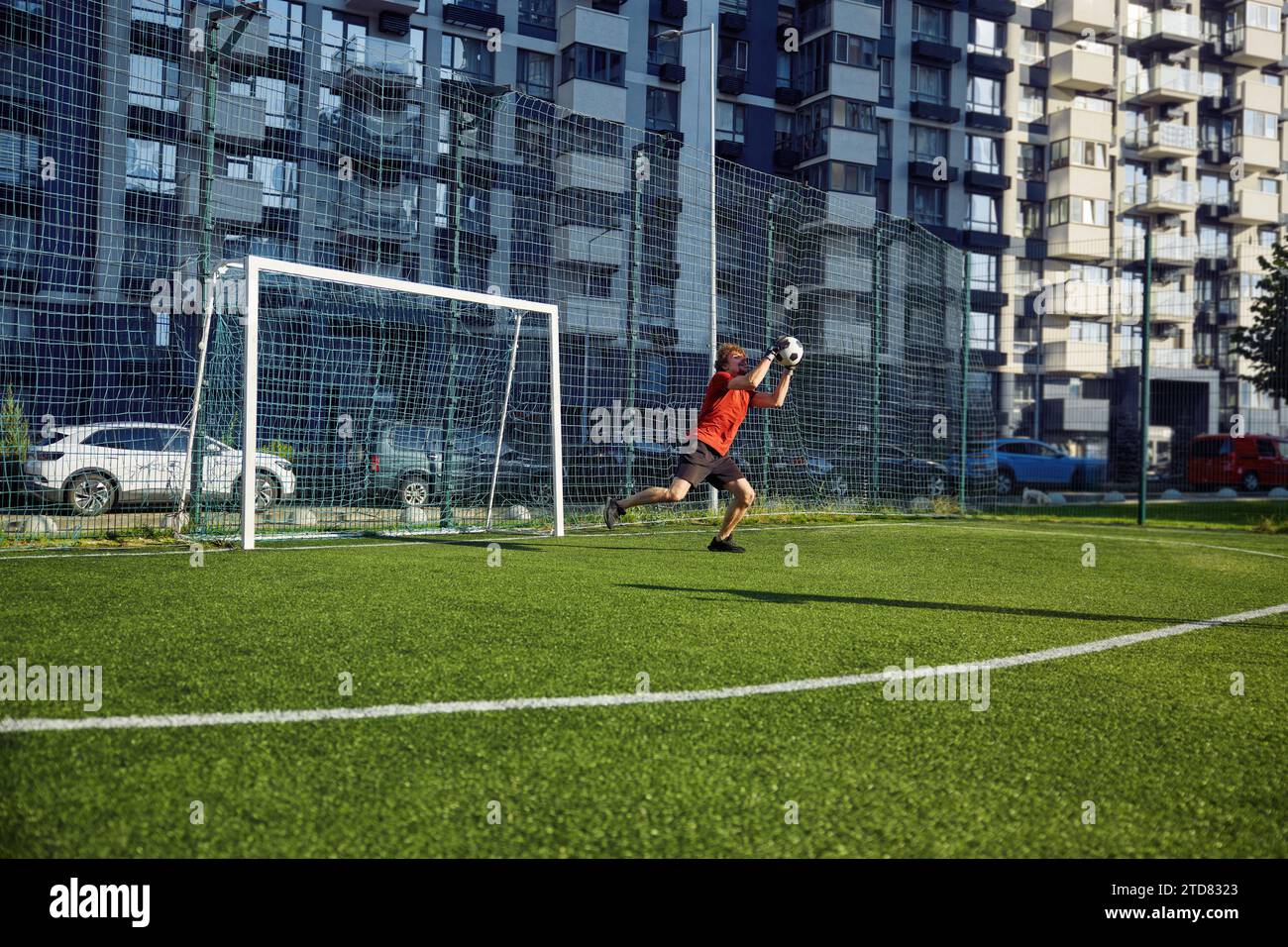 Jeune homme attrapant le ballon de football dans la porte tout en s'entraînant sur le terrain Banque D'Images