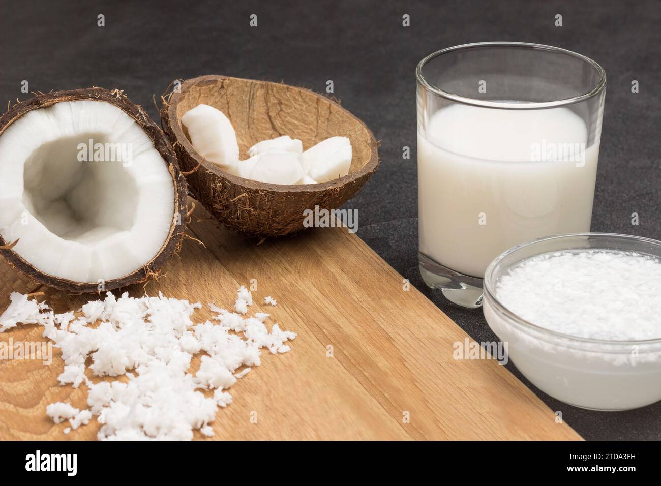 Lait de coco en verre et bol. Flocons de noix de coco, demi-noix de coco fraîche, coquilles de noix de coco à bord. Fond noir. Gros plan Banque D'Images