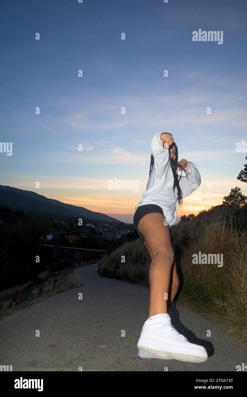 Jeune fille dansant le funk heureux avec la semelle de sneaker vue de dessous à l'extérieur au coucher du soleil Banque D'Images