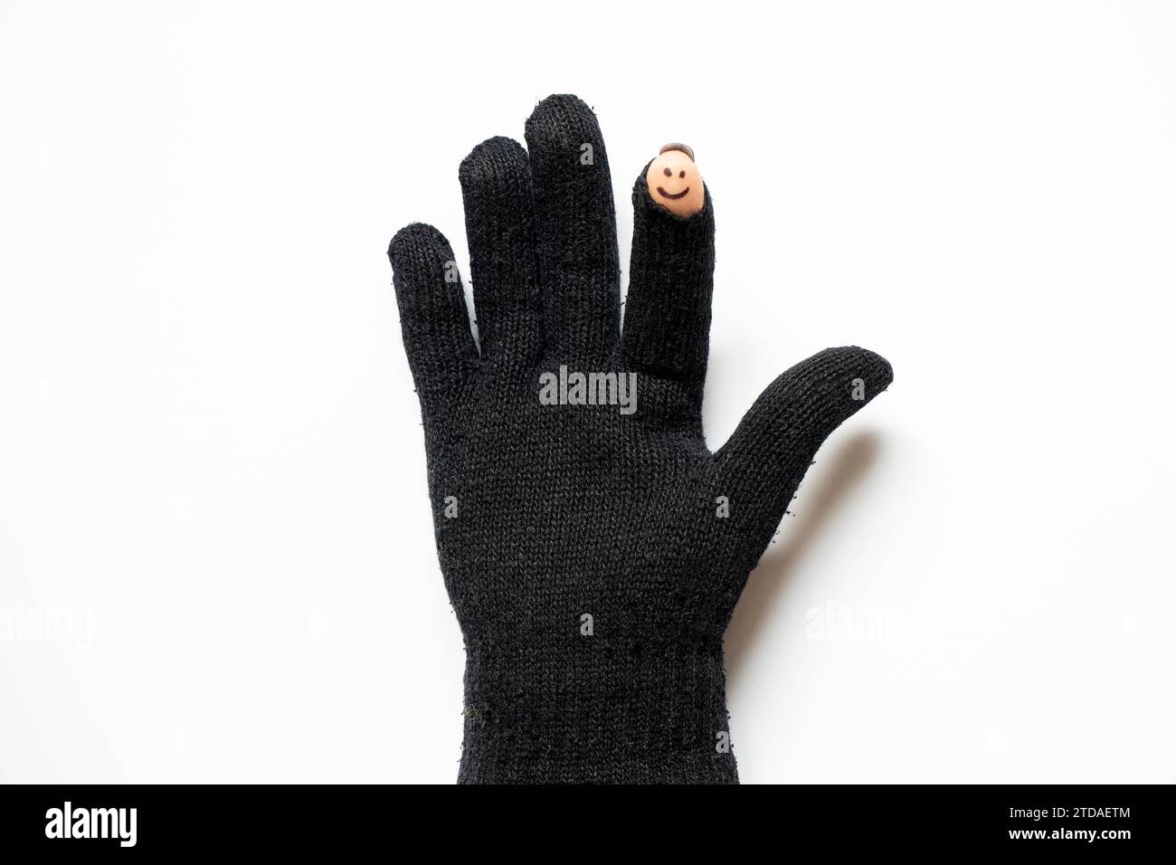 Un gant tricoté noir avec un doigt coupé et un visage souriant joyeux est dessiné sur le doigt, qui est visible depuis le trou dans le gant sur un dos blanc Banque D'Images