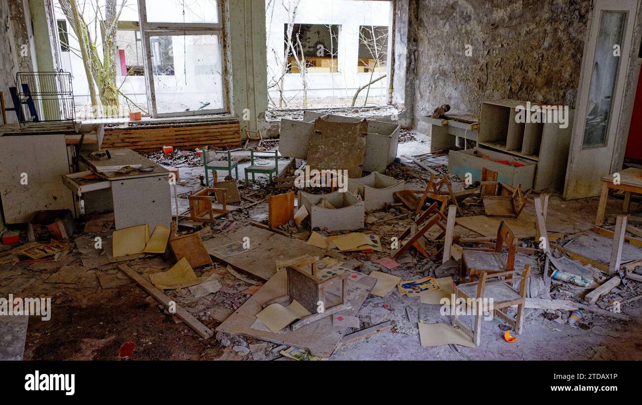 L'image montre une pièce délabrée avec des meubles éparpillés, des débris et des murs écaillés. Les fenêtres sont sales et cassées. Banque D'Images