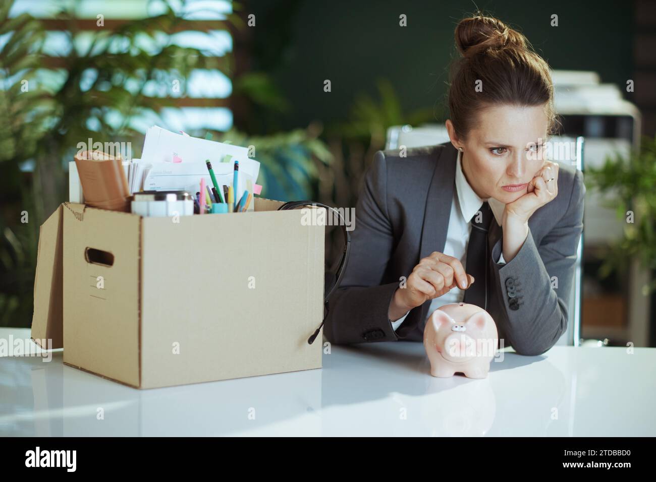 Nouveau travail. pensive moderne 40 ans femme employée dans le bureau vert moderne en costume d'affaires gris avec des effets personnels dans la boîte en carton mettant coi Banque D'Images