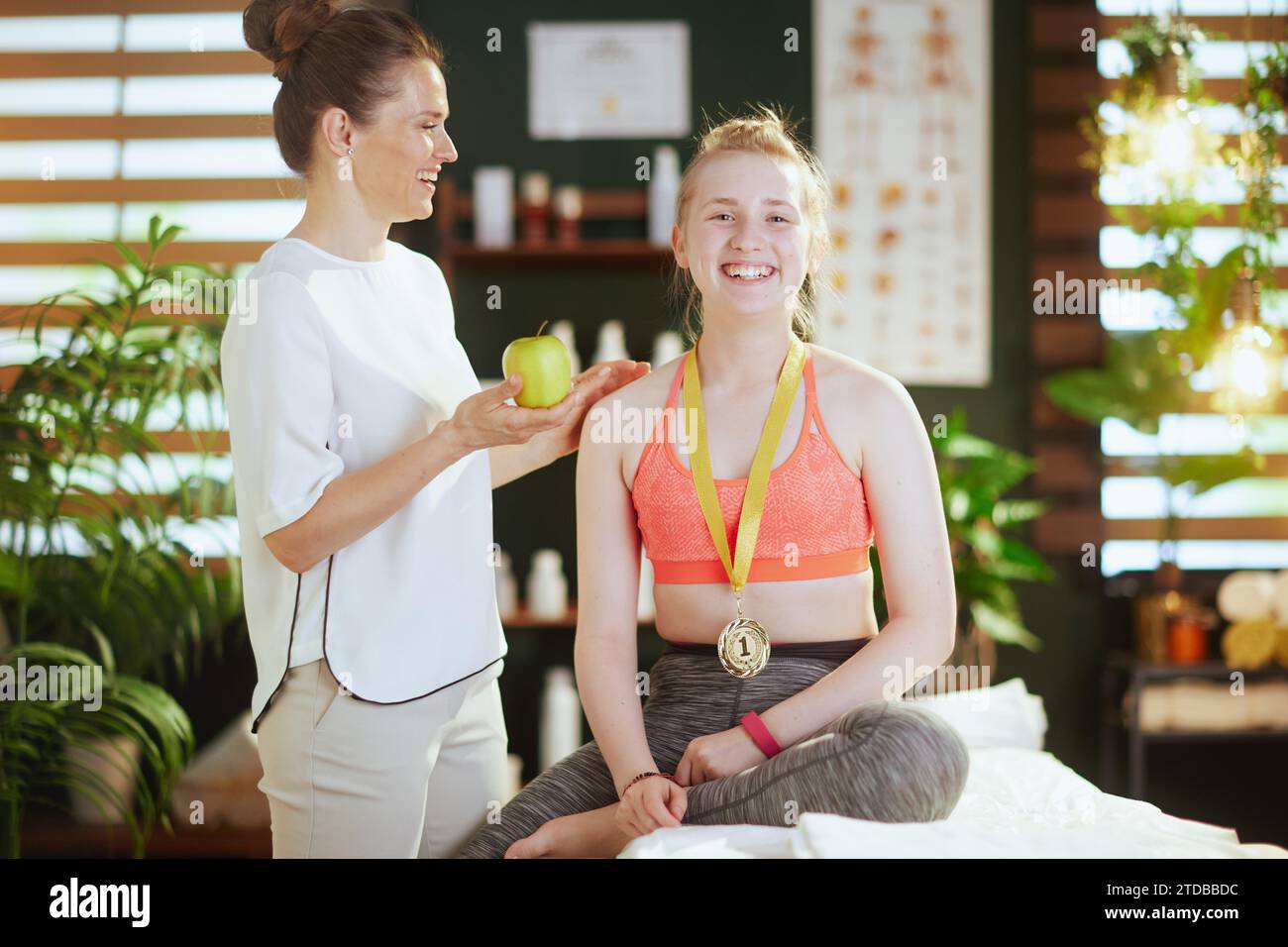 Le temps des soins de santé. femme thérapeute de massage souriant dans l'armoire de massage avec le client adolescent, une pomme et médaille d'or. Banque D'Images