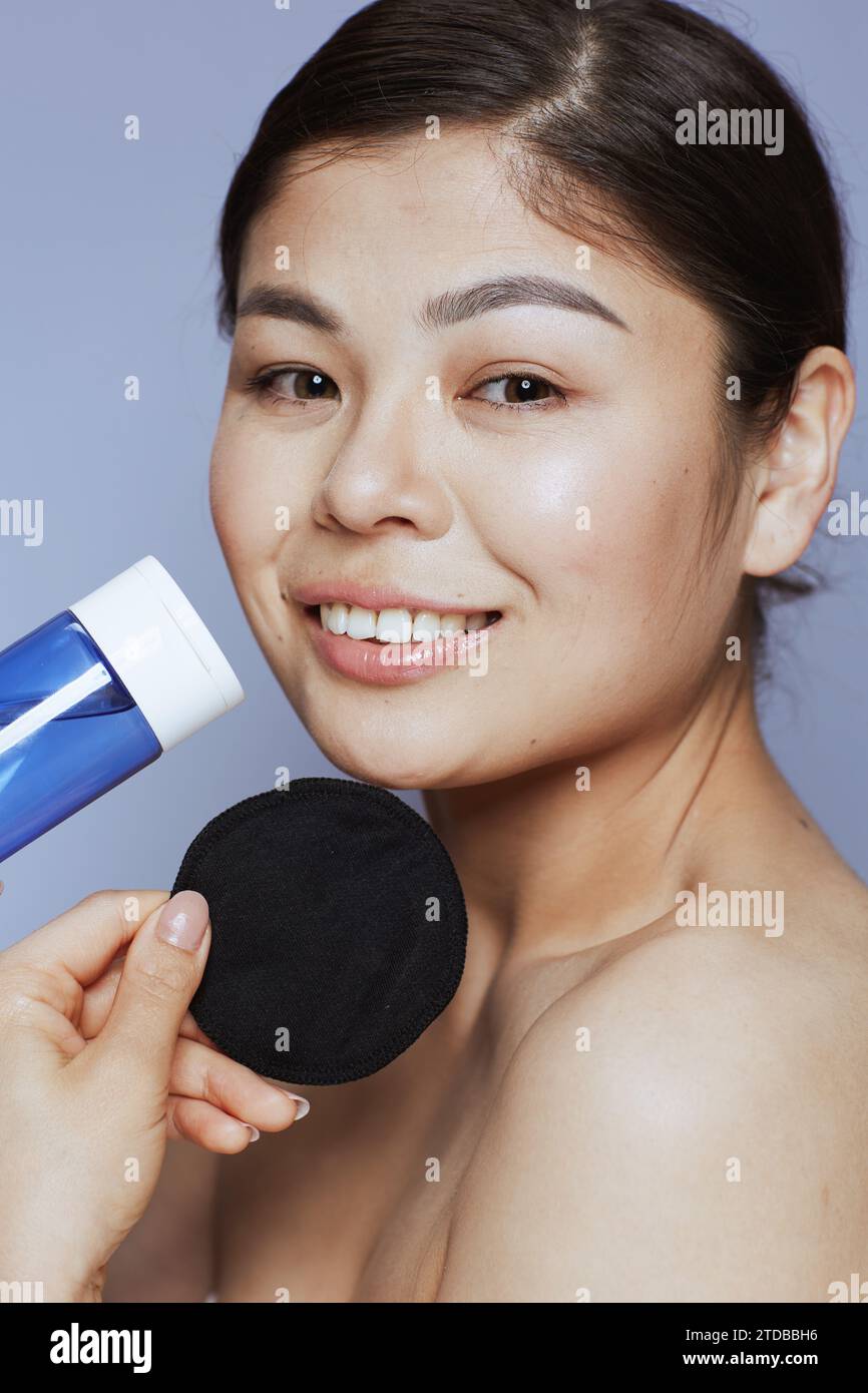 Portrait d'une femme asiatique moderne avec démaquillant et coussin en coton noir sur fond bleu. Banque D'Images