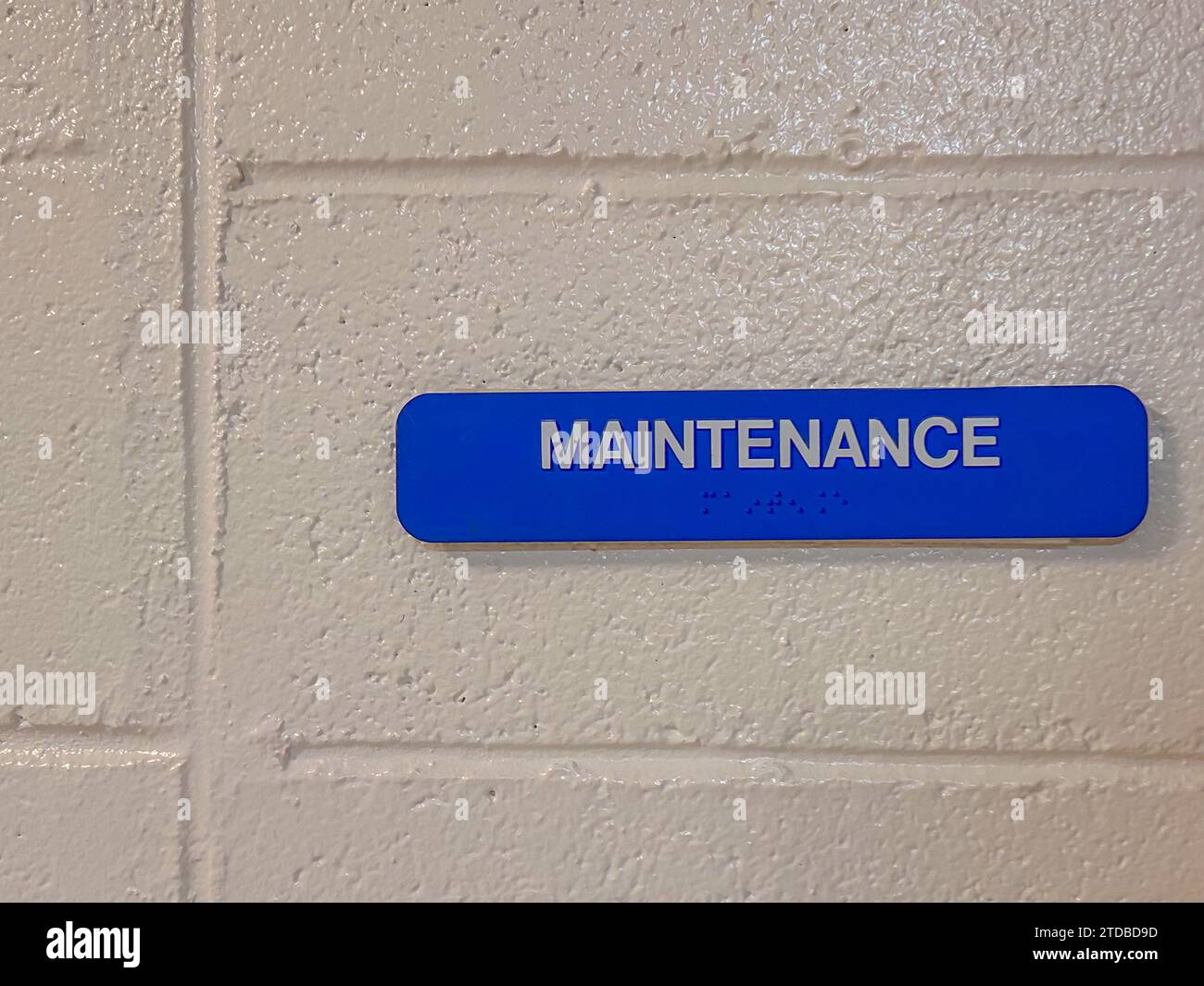 Panneau d'entretien bleu avec braille, sur mur peint en bloc blanc. Banque D'Images