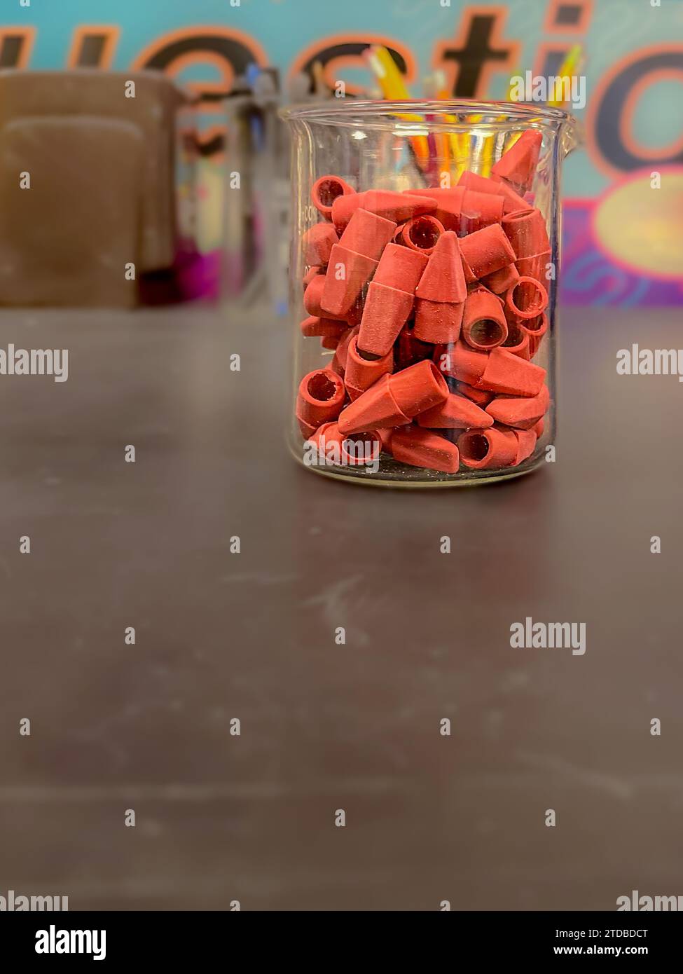 Capuchons de gomme rose dans un bécher de laboratoire en verre transparent sur une table noire. Banque D'Images