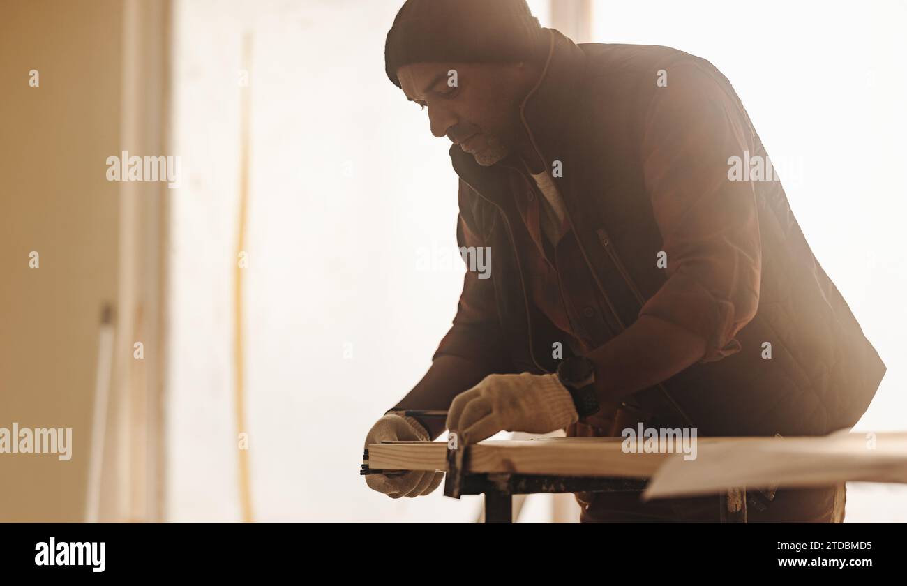 Carpenter mesure une planche de bois pour la rénovation domiciliaire. Travaillant à l'intérieur, le travailleur qualifié remodèle la maison avec précision. Utilisant un ruban à mesurer, lui Banque D'Images