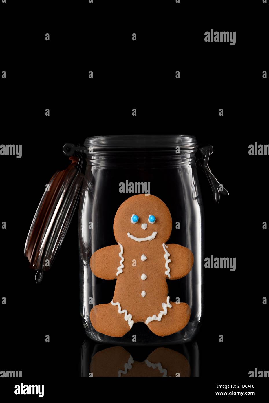 Un pot de stockage ou de mise en conserve en verre avec un biscuit Gingerbread Man décoré isolé sur noir avec réflexion, avec couvercle ouvert. Banque D'Images