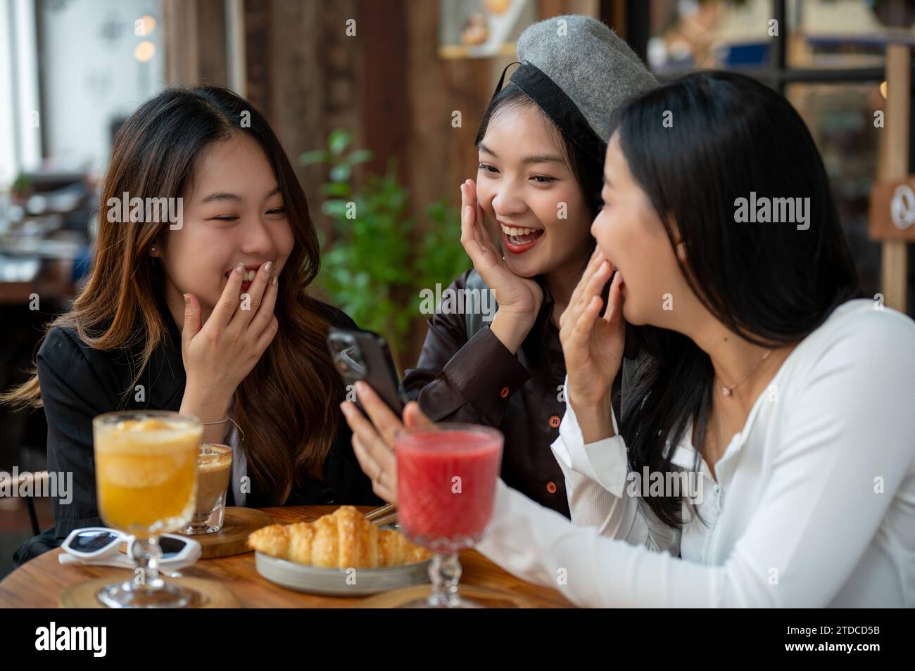 Groupe d'amies asiatiques joyeuses et attrayantes apprécient traîner dans un café ou un restaurant dans la ville ensemble, chit bavarder, regarder somet Banque D'Images