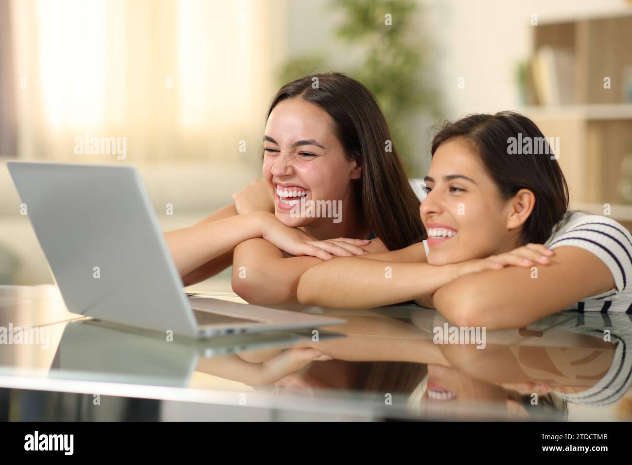 Deux femmes heureuses riant en regardant les médias sur ordinateur portable à la maison Banque D'Images