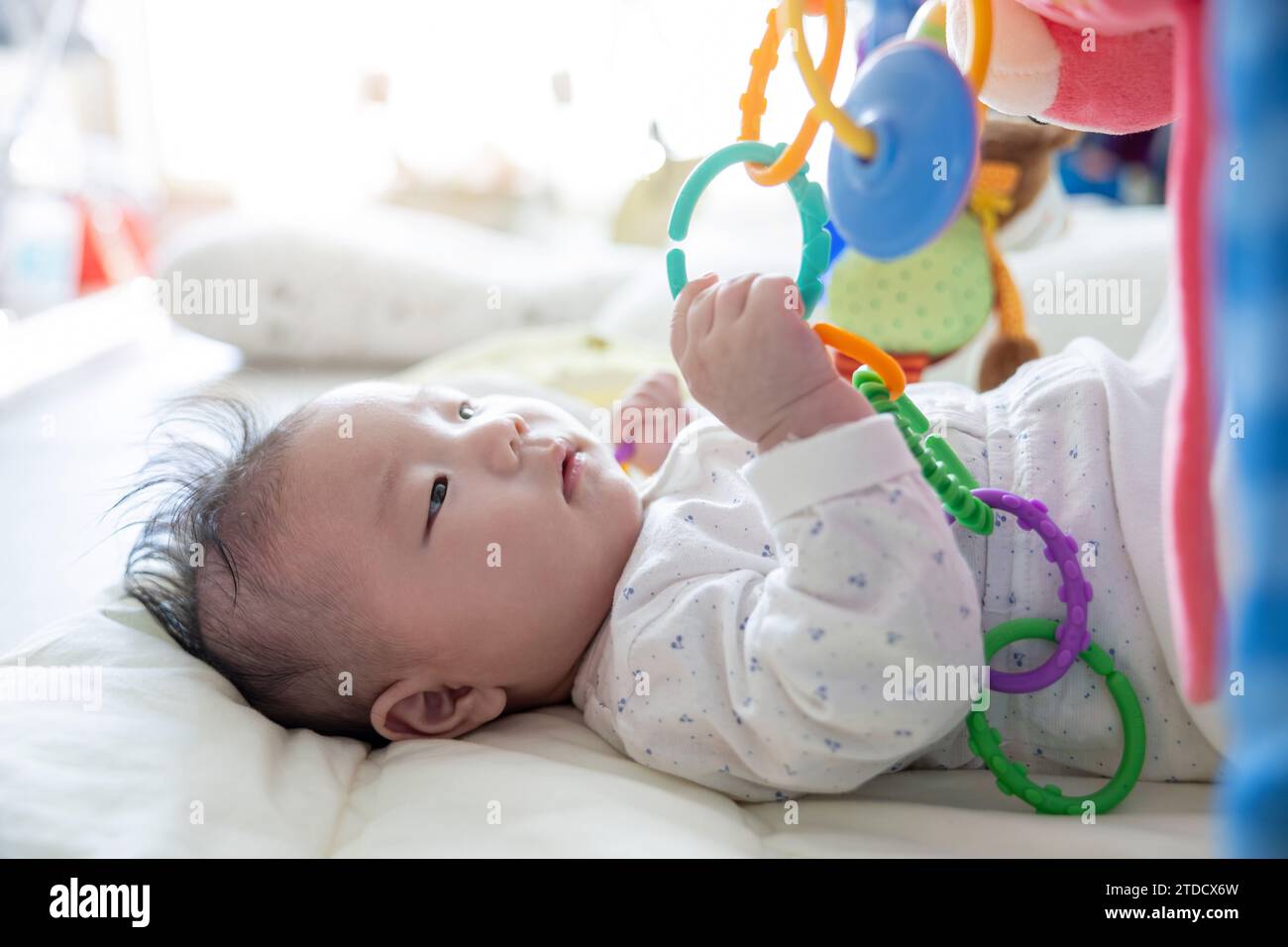 Un bébé qui n'a que quelques jours est allongé à côté d'une fenêtre ensoleillée et joue avec des jouets Banque D'Images