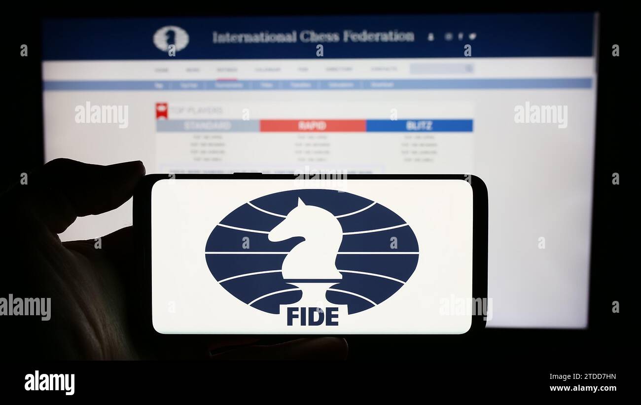 Personne détenant un téléphone portable avec le logo de l'organisation Fédération internationale des échecs (FIDE) devant la page Web. Concentrez-vous sur l'affichage du téléphone. Banque D'Images