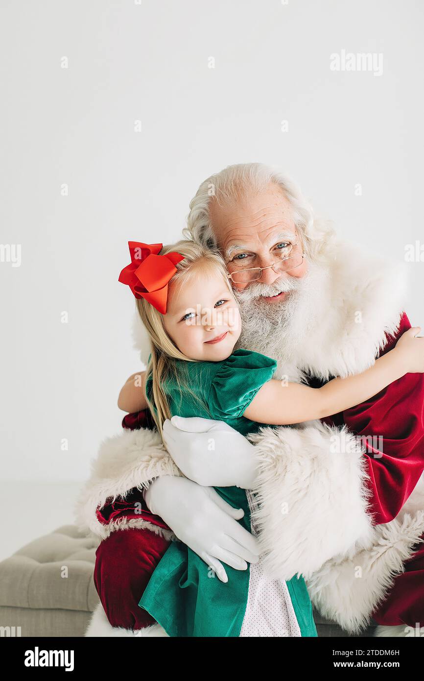 Petite fille avec un arc dans ses cheveux embrassant le père noël Banque D'Images